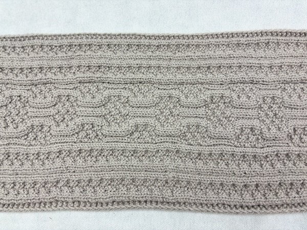 Close-up of flat knitted scarf panel showing cable repeats and seed-like texture