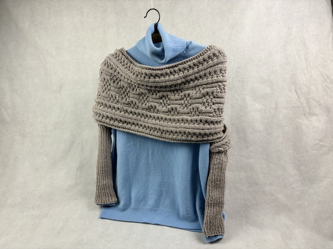 Neutral textured knit wrap with integrated sleeves styled over a light blue turtleneck on a hanger