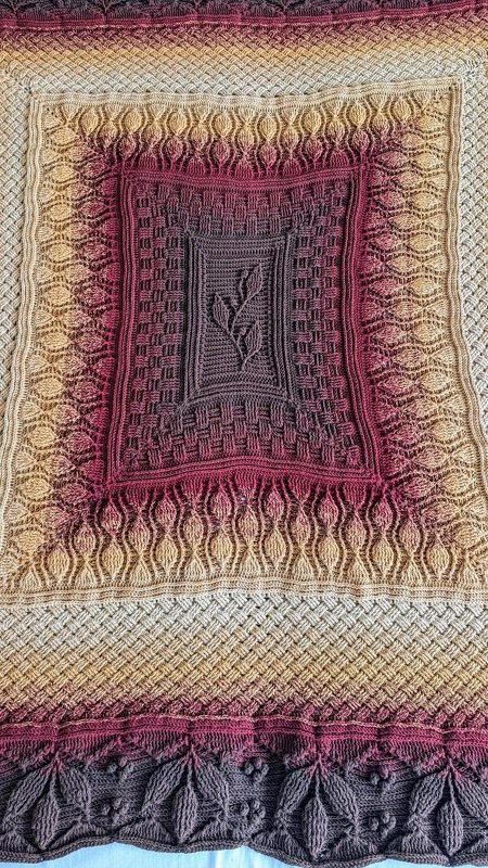 Gehäkelte Decke in Beige, Bordeaux und Braun mit zentralem Blattmotiv und Reliefmuster.