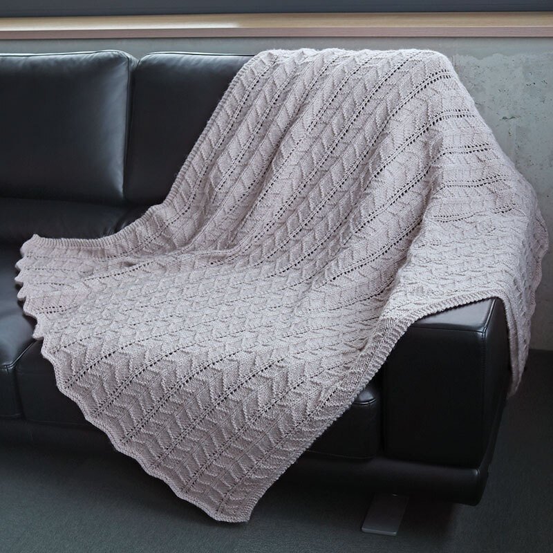 Hellbeige gestrickte Decke mit Zopf- und Ajourmuster auf dunkler Ledercouch