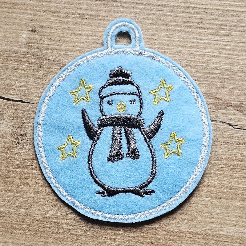 Runder hellblauer Filzanhänger mit besticktem Pinguin, Mütze, Schal und gelben Sternen