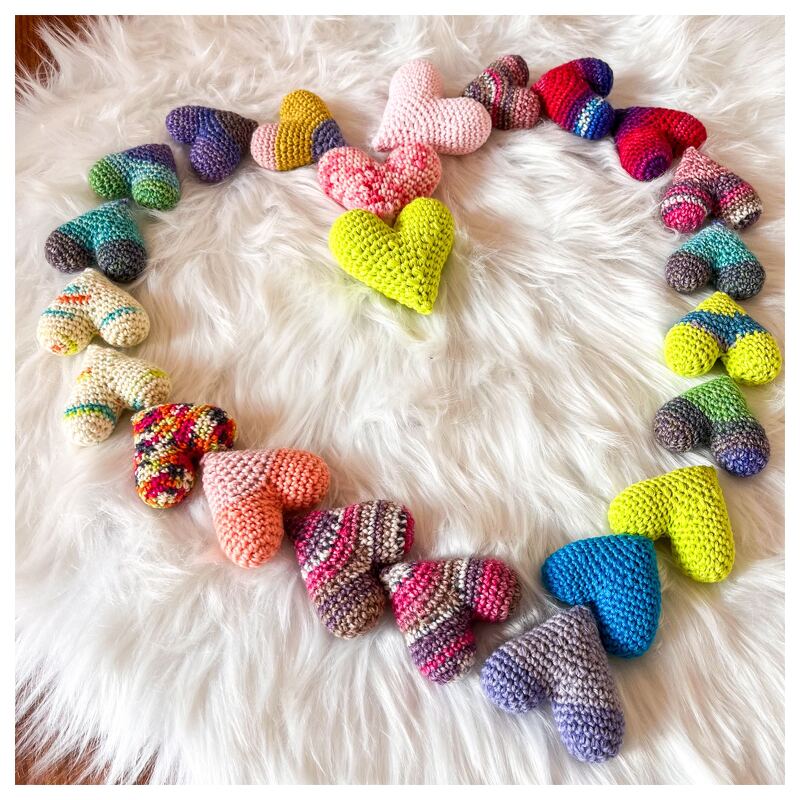 Bunte gehäkelte Mini‑Herzen auf weißem Fell