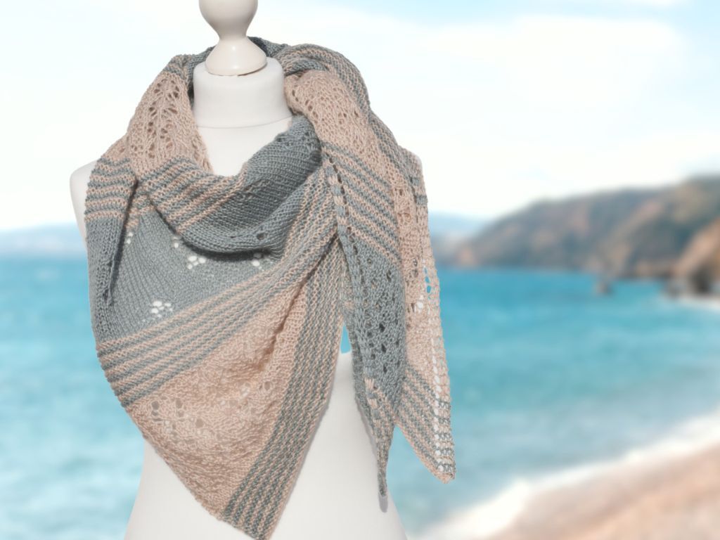 Gestricktes Dreieckstuch in Grau und Beige mit Streifen und Ajourmuster auf weißer Schneiderpuppe vor Meer