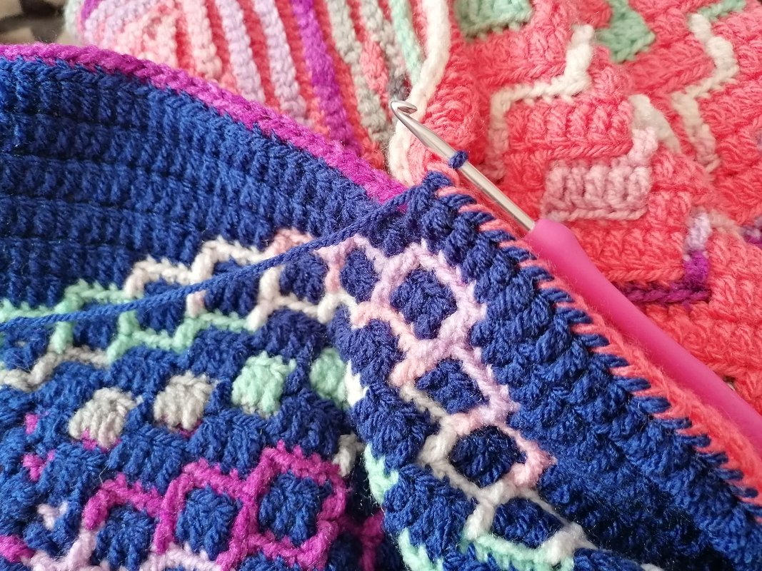 Nahaufnahme einer bunten Häkeldecke mit laufender Häkelnadel