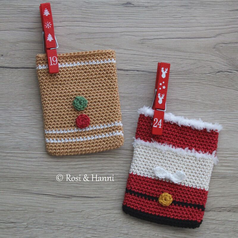 Zwei gehäkelte Adventssäckchen, Lebkuchenmann-Design und Weihnachtsmann-Design, mit roten nummerierten Klammern auf Holzuntergrund.