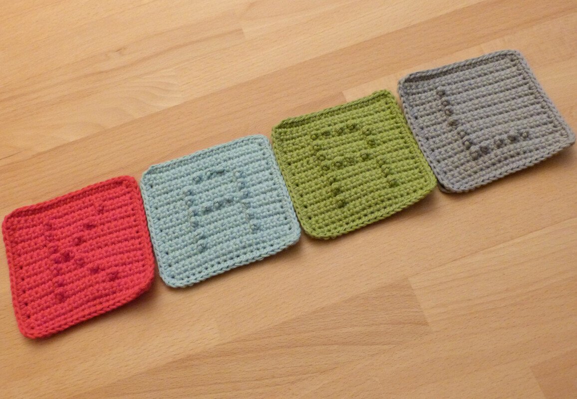 Vier gehäkelte Quadrate in Rot, Hellblau, Grün und Grau mit den Buchstaben L, O, V, E.