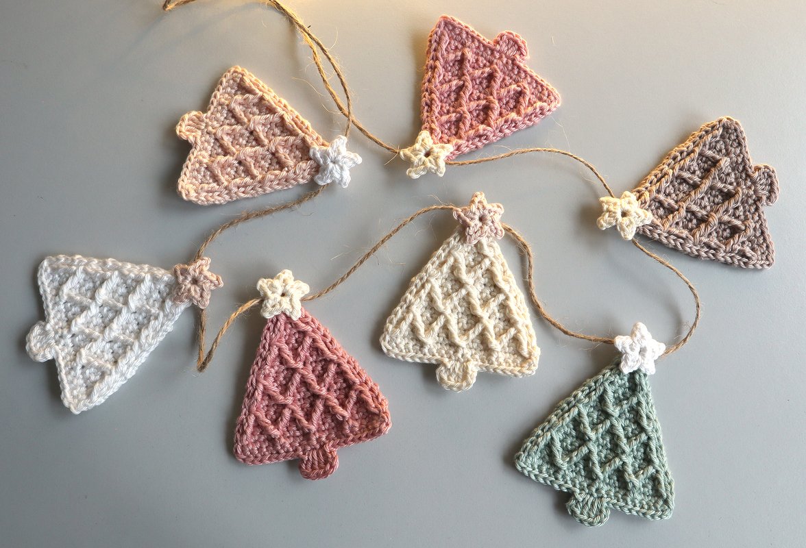 Small crochet Christmas tree ornaments in pastel colors attached to jute twine with star connectors