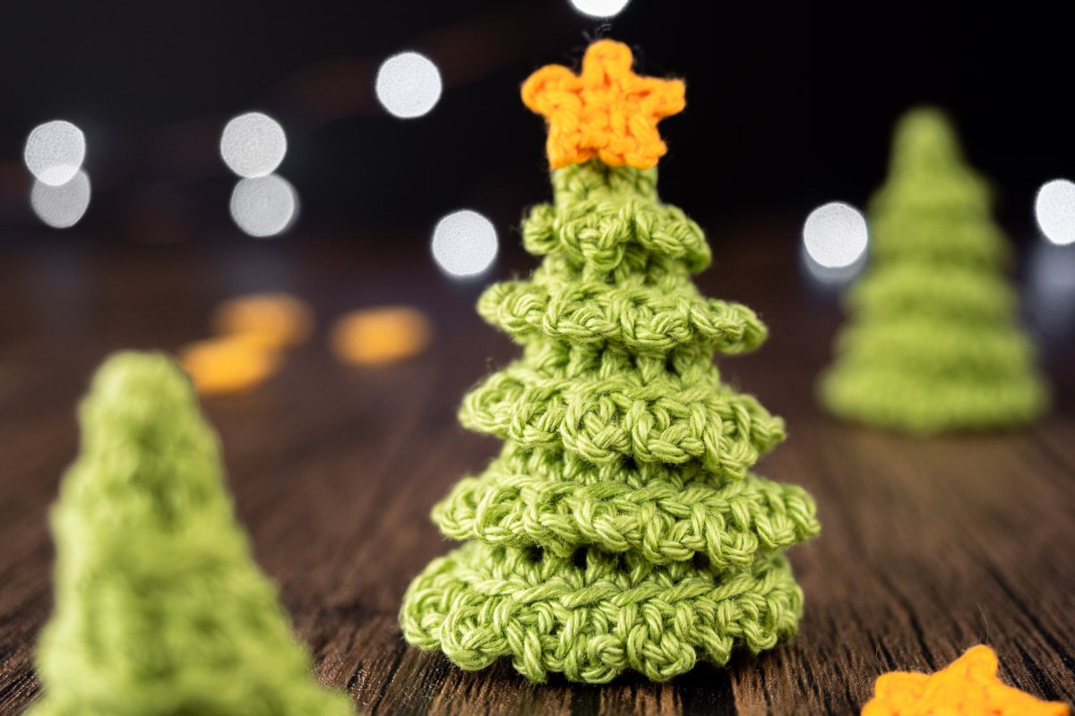 Kleiner gestufter Häkel-Tannenbaum aus grünem Garn mit orangem Stern vor unscharfem Lichterhintergrund