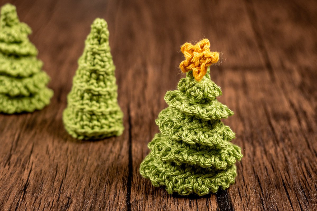 Drei kleine gehäkelte Weihnachtsbäume auf Holz; vorderster mit gelbem Stern.