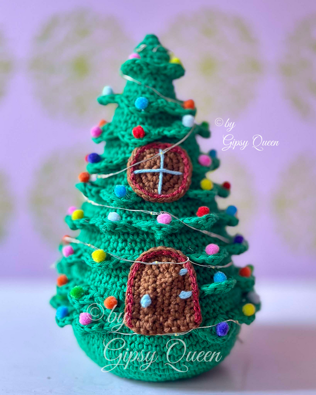 Grüner gehäkelter Weihnachtsbaum mit farbigen Pompons, feiner Lichterkette und runden sowie bogenförmigen Applikationen.