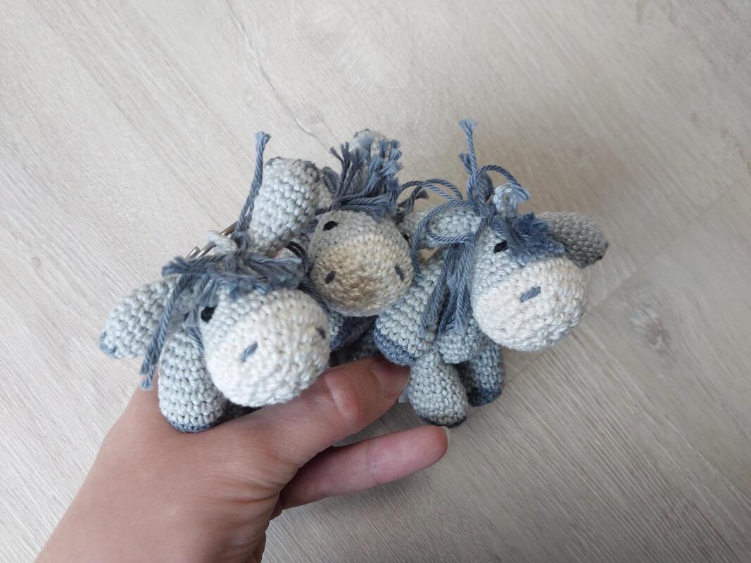 Drei gehäkelte Amigurumi‑Esel in Grau‑Blau, gehalten in einer Hand