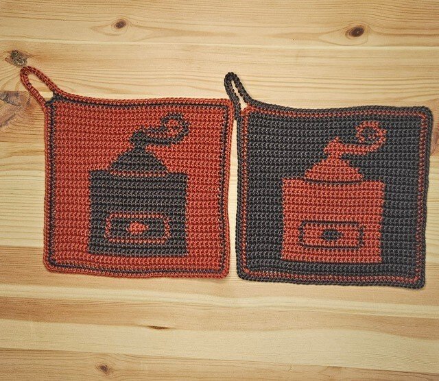 Zwei gehäkelte quadratische Topflappen mit Kaffeemühlen-Motiv in invertierten Farben auf Holzuntergrund