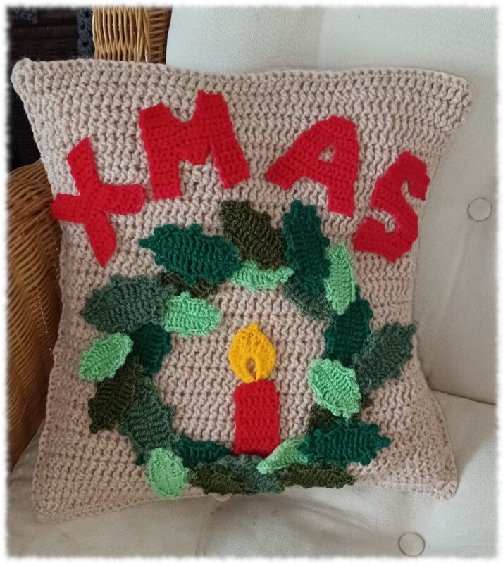 Beiges gehäkeltes Kissen mit rotem XMAS-Schriftzug, grünem Kranz und roter Kerze
