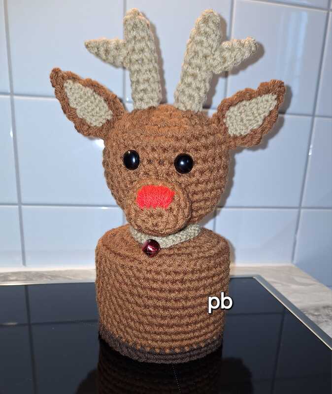 Gehäkeltes Rentier mit roter Nase, hellbraunen Geweihen und Glöckchen auf zylindrischem Sockel