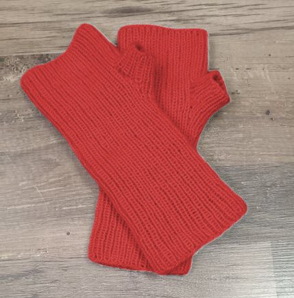 Rote gestrickte Armstulpen mit Rippenmuster und Daumenloch auf Holzuntergrund
