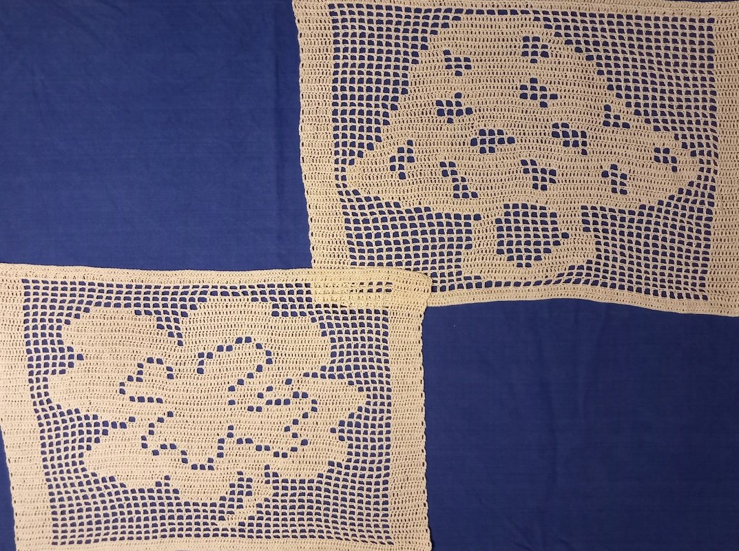 Zwei ecrufarbene, rechteckige Filet-Häkeldeckchen mit Blumenmotiven auf blauem Untergrund