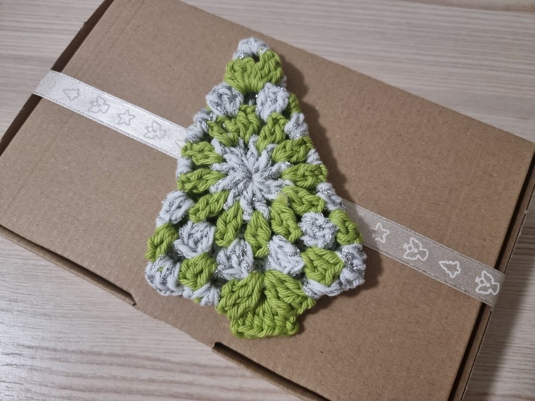 Gehäkelter Weihnachtsbaum in Grün und Silber auf brauner Geschenkbox mit Band.