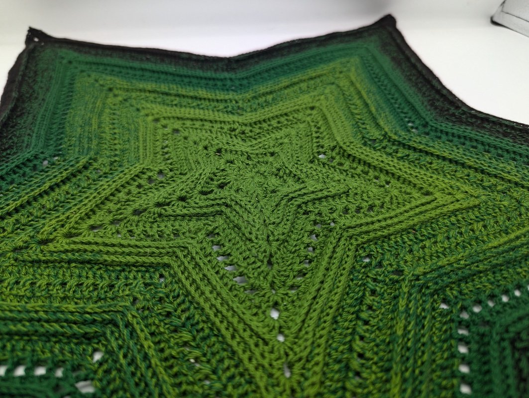 Gehäkeltes sternförmiges Deckchen in verschiedenen Grüntönen mit sichtbaren Rippenreihen