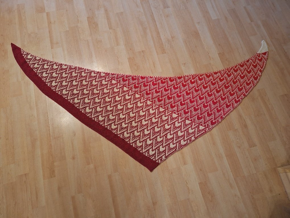 Gestricktes Dreieckstuch in Rot und Creme mit Zickzackmuster, flach auf hellem Holzboden ausgebreitet