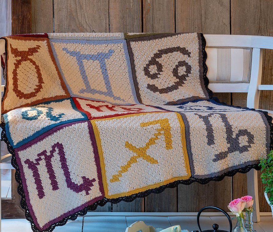 Modulare gehäkelte Decke aus Einzelquadraten mit Tierkreis-Symbolen und dunkler Abschlusskante