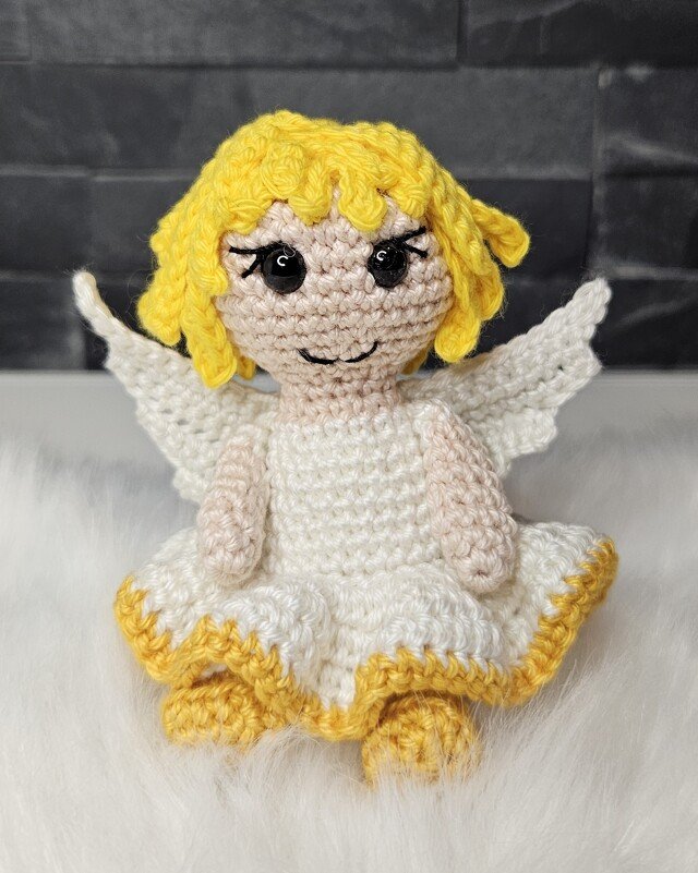 Gehäkeltes Amigurumi-Engelchen mit gelben Haaren, weißen Flügeln und weißem Kleid mit gelbem Saum