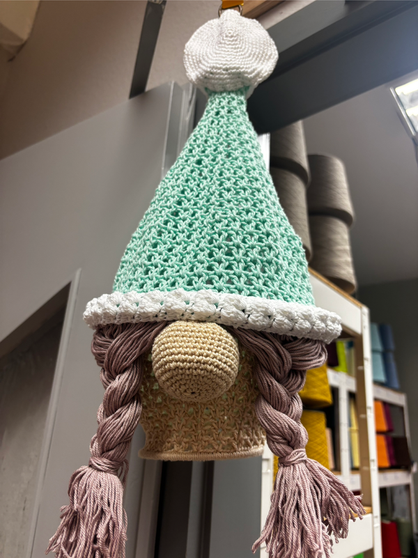 Handgehäkelter Wichtel mit mintgrüner Zipfelmütze, weißem Bommel, beiger Nase und langen rosa Zöpfen.