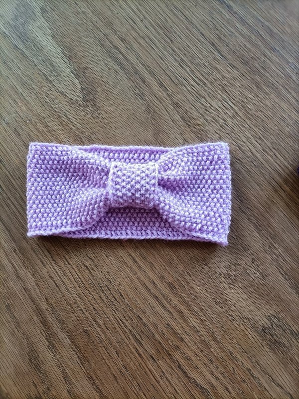 Helllila gestricktes Stirnband mit mittigem Knoten auf Holzuntergrund