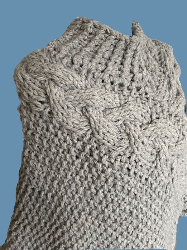 Nahaufnahme eines grauen gestrickten Damenpullovers mit Zopf- und Strukturmuster