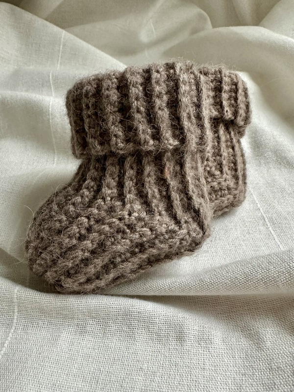 Gehäkelter Baby-Bootie in Braun mit breitem Rippbündchen auf hellem Stoff
