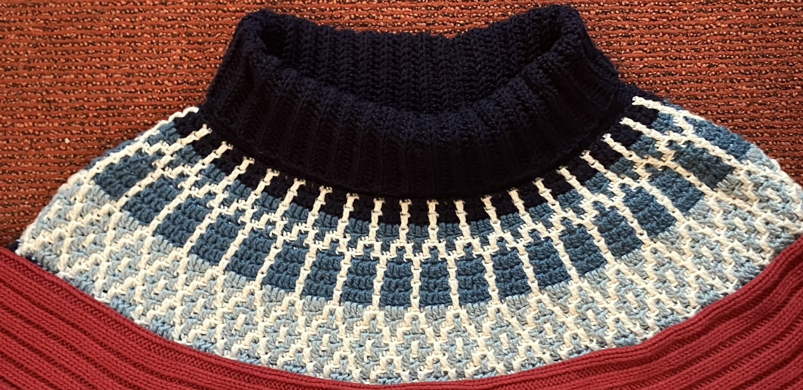 Gehäkelter Rollkragenpullover mit blau-weißem geometrischem Muster und rotem Saum