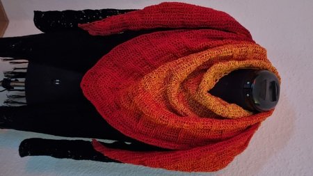 Crochet triangle shawl with red-to-orange gradient draped on a black dress form.