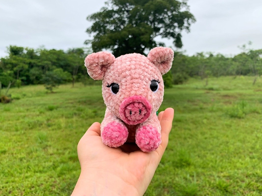 Rosa kuscheliges Amigurumi-Glücksschweinchen, handgehalten vor Naturhintergrund