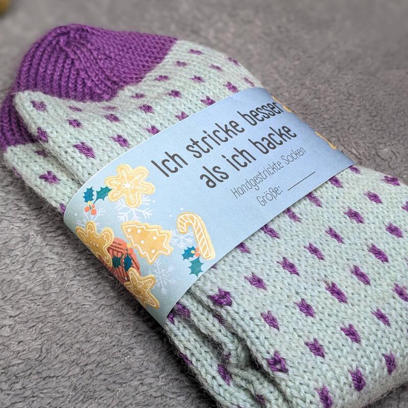 Gefaltete handgestrickte Damensocken hellgrün mit violetten Punkten und einem blauen Etikett mit weihnachtlichen Motiven