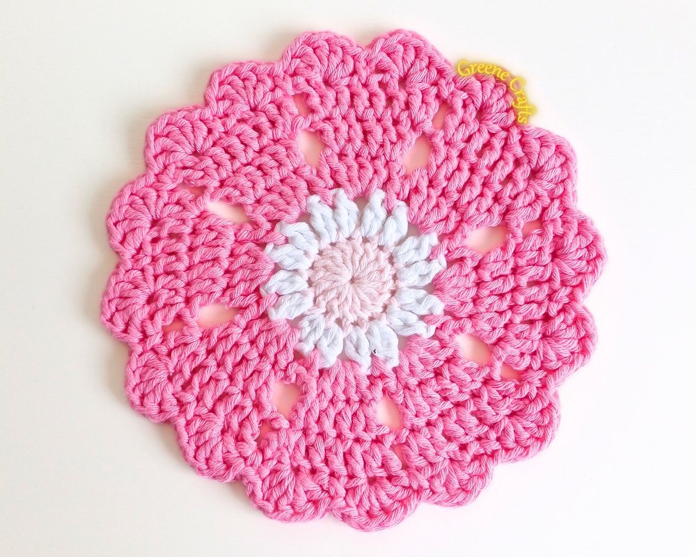 Round pink crocheted potholder with white daisy center and scalloped edge