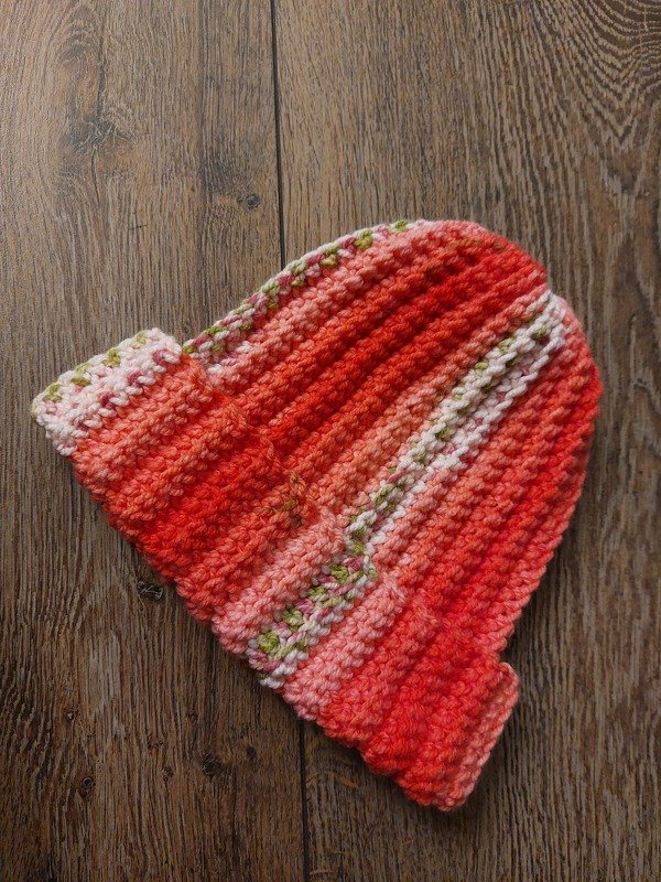 Handgehäkelte Mütze in Orange, Rosa und Grün auf Holz
