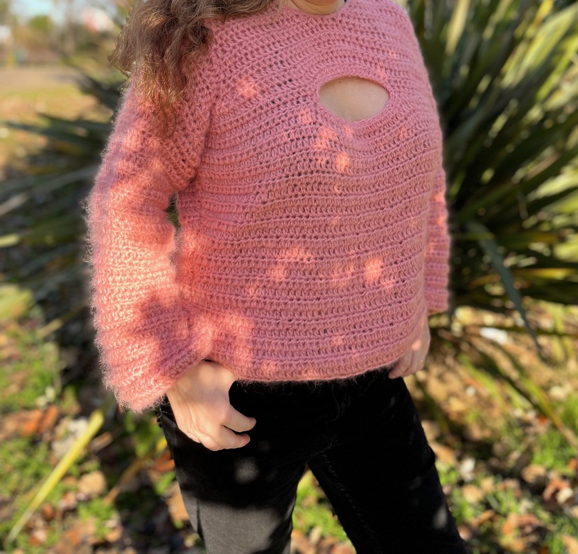 Close-up of a fuzzy pink crochet sweater with a round keyhole neckline.