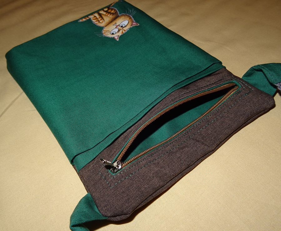 Grüne Stofftasche mit orangefarbenem Cartoon-Katzenmotiv und braunem Reißverschlussfach