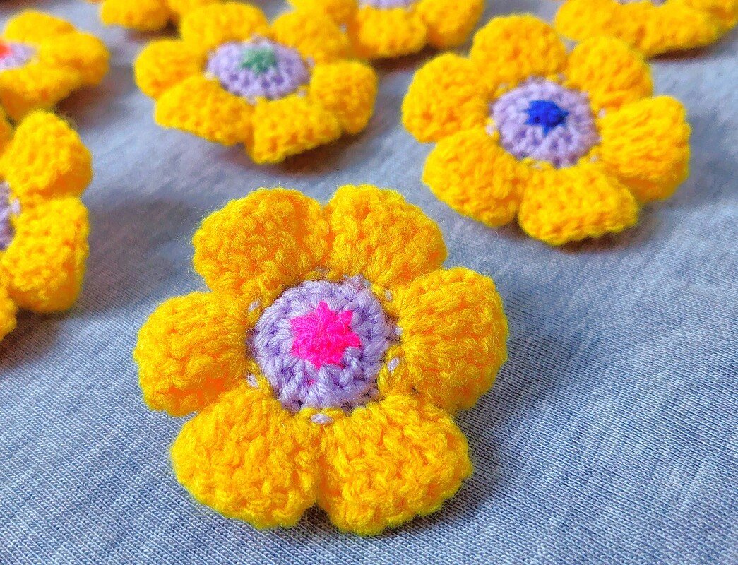 Handgehäkelte gelbe Blumen mit bunten Mitteln auf hellblauem Stoff