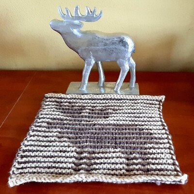 Gestricktes Streifenquadrat in Naturtönen auf Holztisch mit silberner Hirschfigur