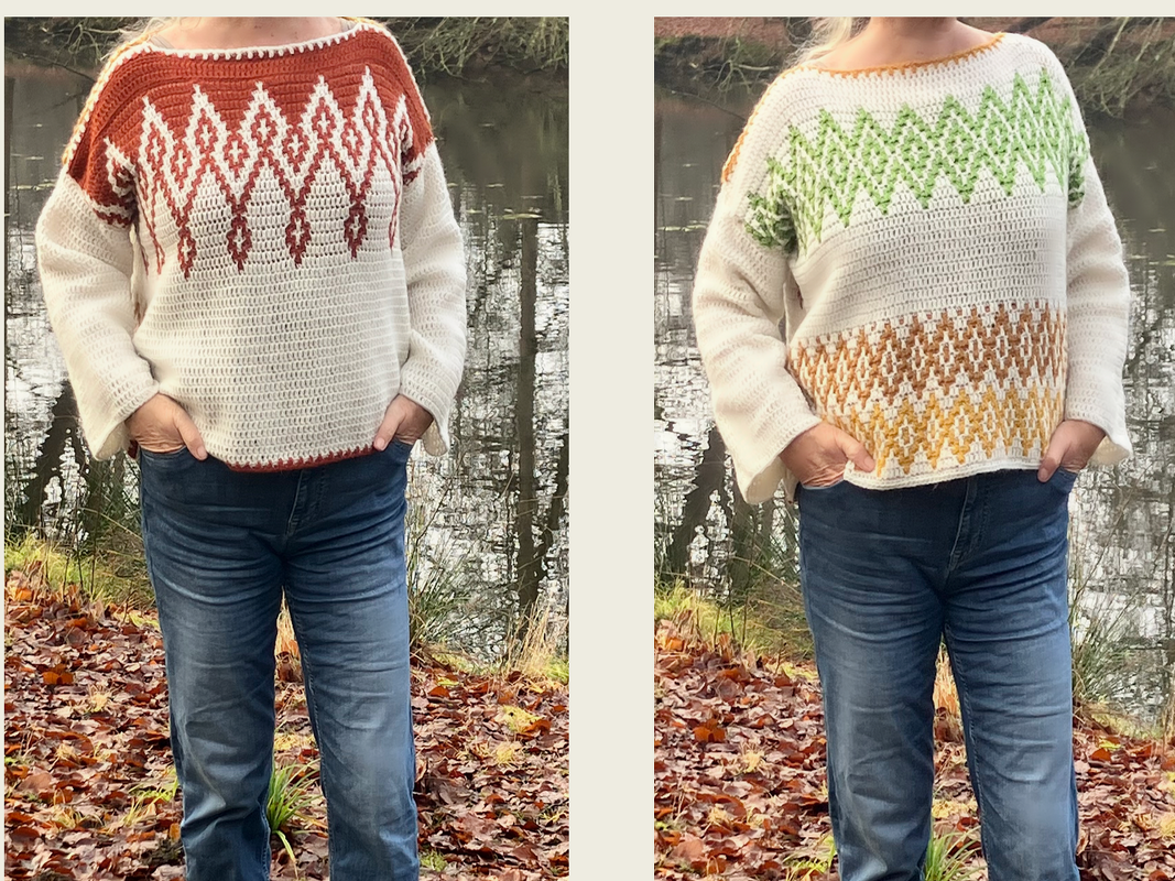 Person in Jeans präsentiert zwei gehäkelte Pullover mit geometrischen Farbmustern vor einem Teich und herbstlichem Laub.