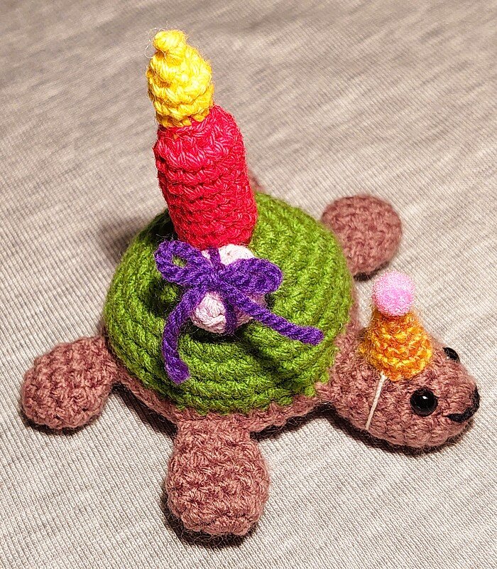 Gehäkelte Schildkröte mit Geburtstagskerze und Partyhut auf neutralem Hintergrund