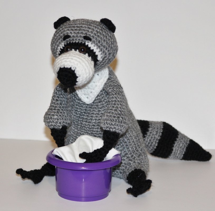 Gehäkelter Amigurumi-Waschbär grau-schwarz mit gestreiftem Schwanz und lila Schüssel