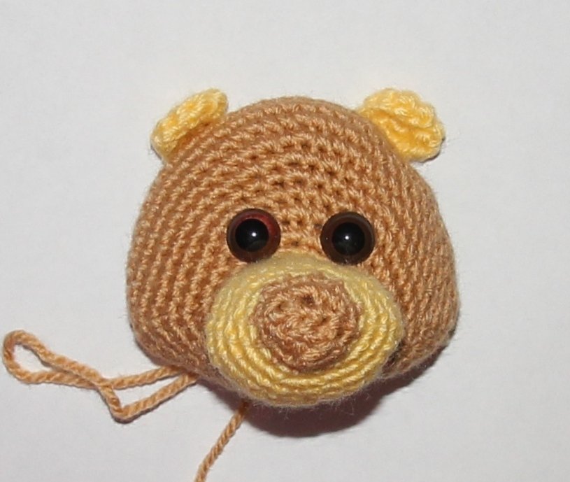 Gehäkelter Amigurumi-Bärenkopf in Braun mit gelber Schnauze und runden dunklen Augen