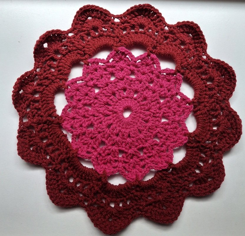 Round crochet coaster with pink center and burgundy scalloped outer edge