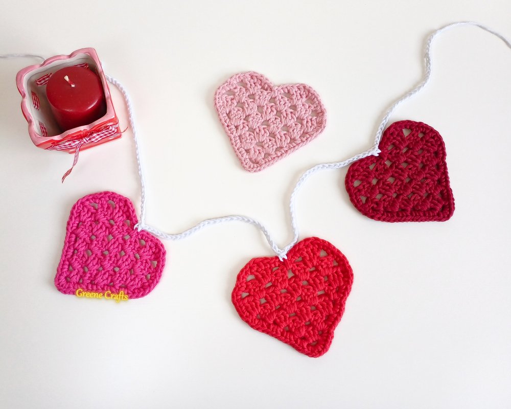 Crocheted heart garland with red and pink hearts linked by a white chain on a light surface.
