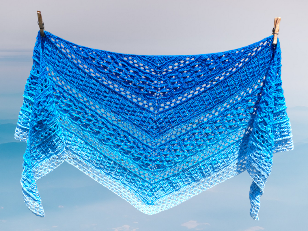 Gehäkeltes blaues Dreieckstuch mit Farbverlauf und offenem Lochmuster an einer Wäscheleine vor klarem Himmel