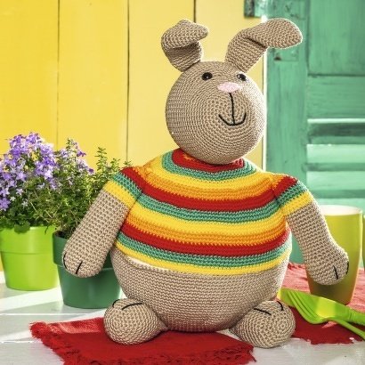 Sitzender gehäkelter Hase mit langen Ohren und buntem Streifenpullover auf einem Tisch