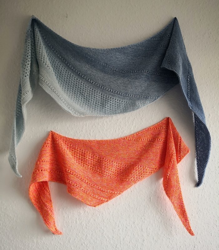 Zwei gestrickte Dreieckstücher an weißer Wand, oben blau-grau, unten orange
