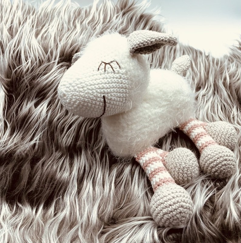 weißes gehäkeltes Schaf Amigurumi liegend auf hellgrauem Felluntergrund