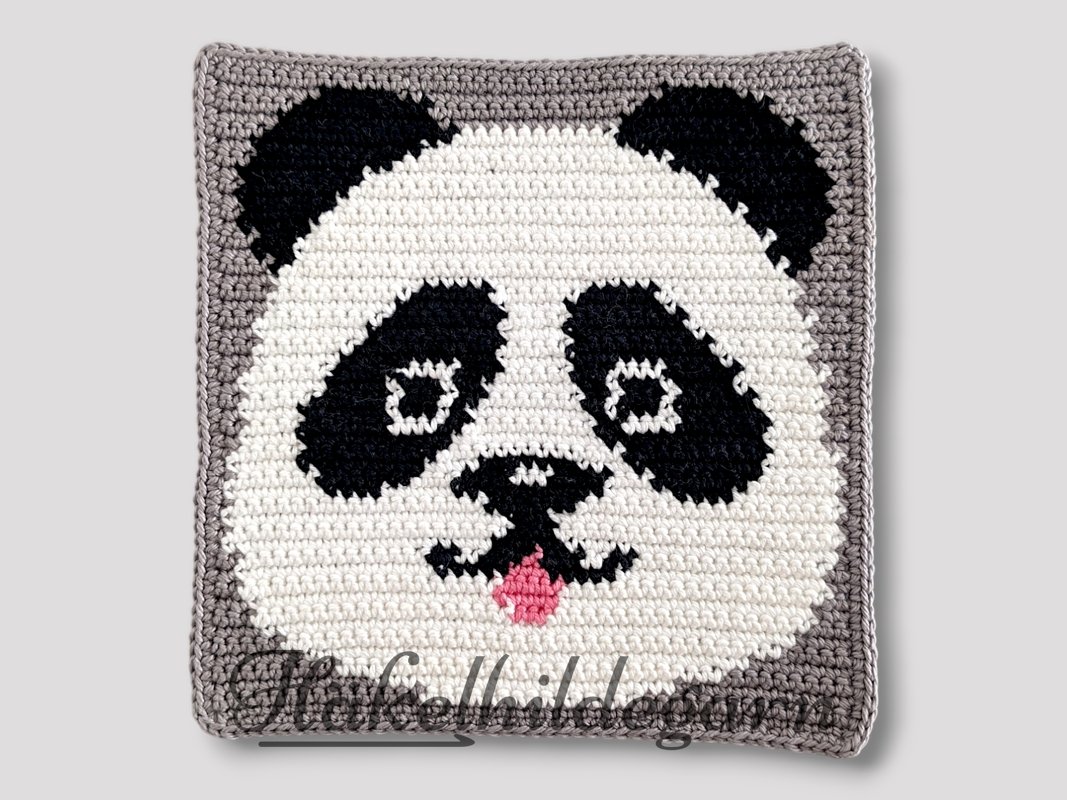 Gehäkeltes Pixelquadrat mit Panda-Gesicht in Weiß, Schwarz, Grau und rosa Zunge